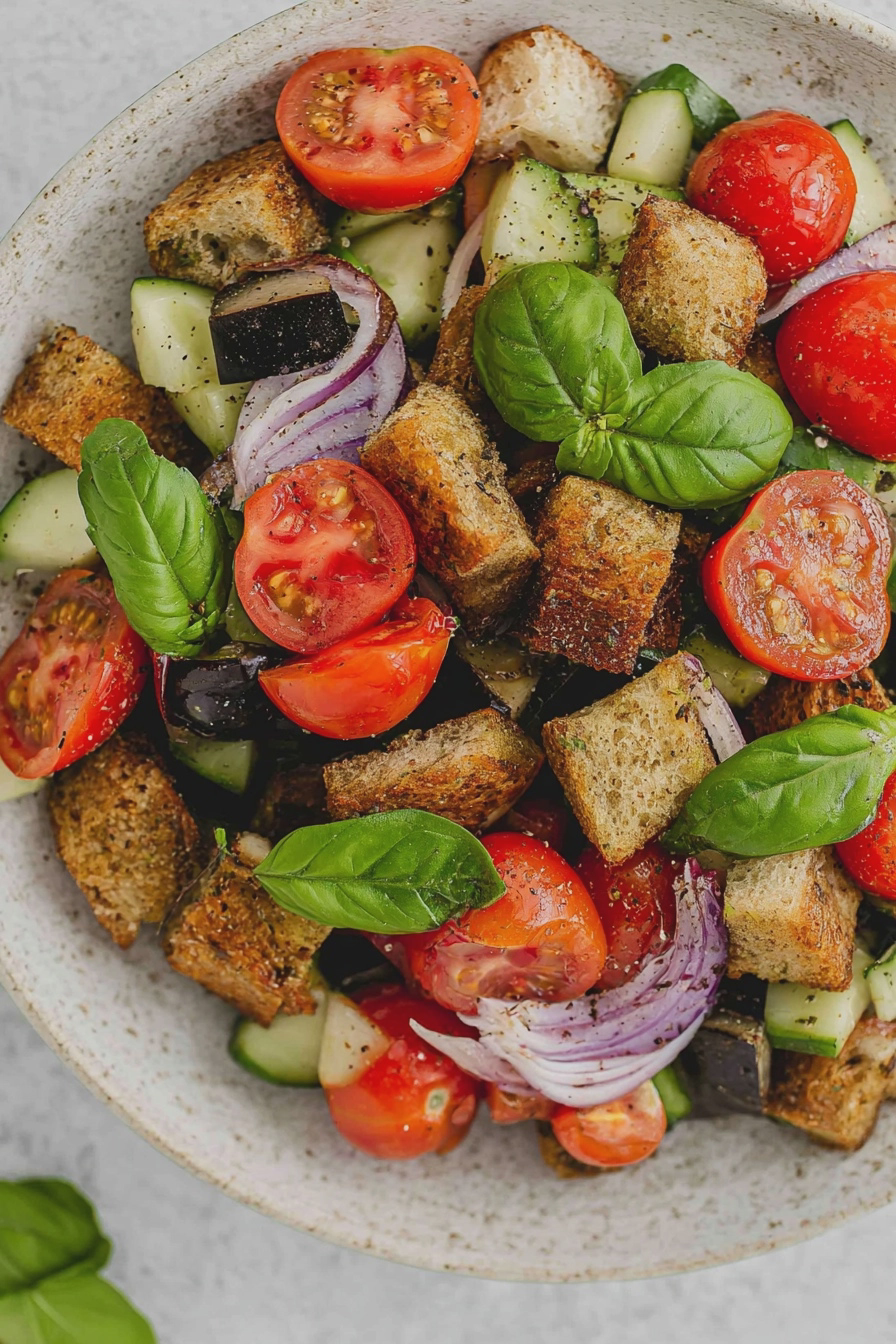Nahaufnahme von Panzanella, einem italienischen Brotsalat mit frischen Tomaten, Gurken und Basilikum auf einem Teller.